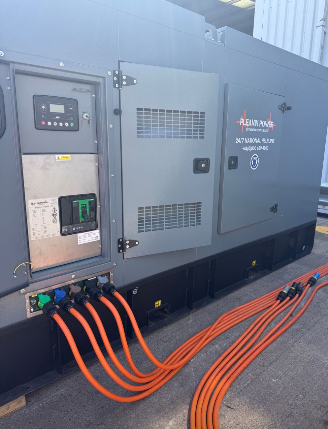 Orange cables lead away from a grey-fronted power generator, with panels viewable for monitoring.