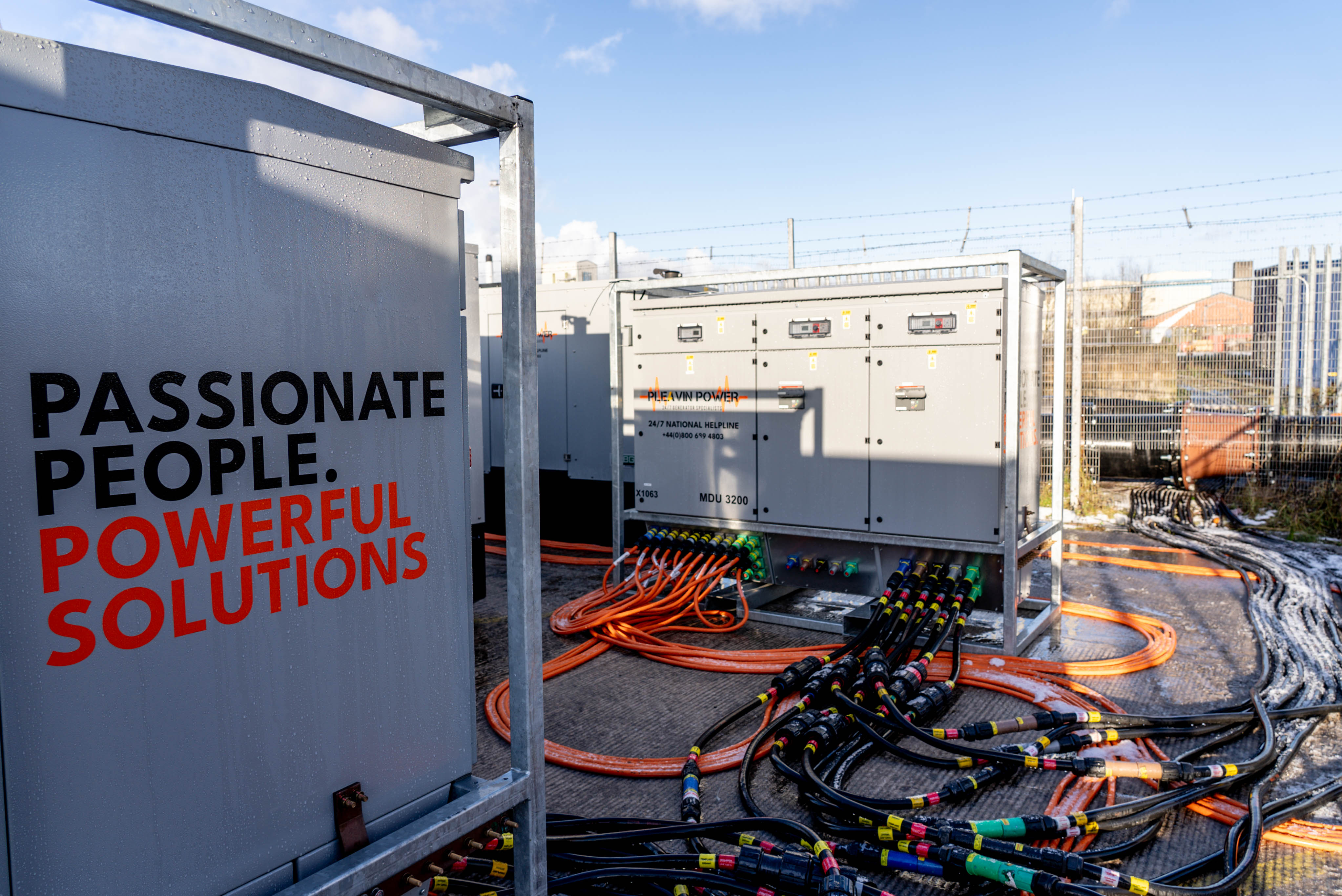 A set of Pleavin Power branded generators set up in a yard, connected with a myriad of red and orange cables.