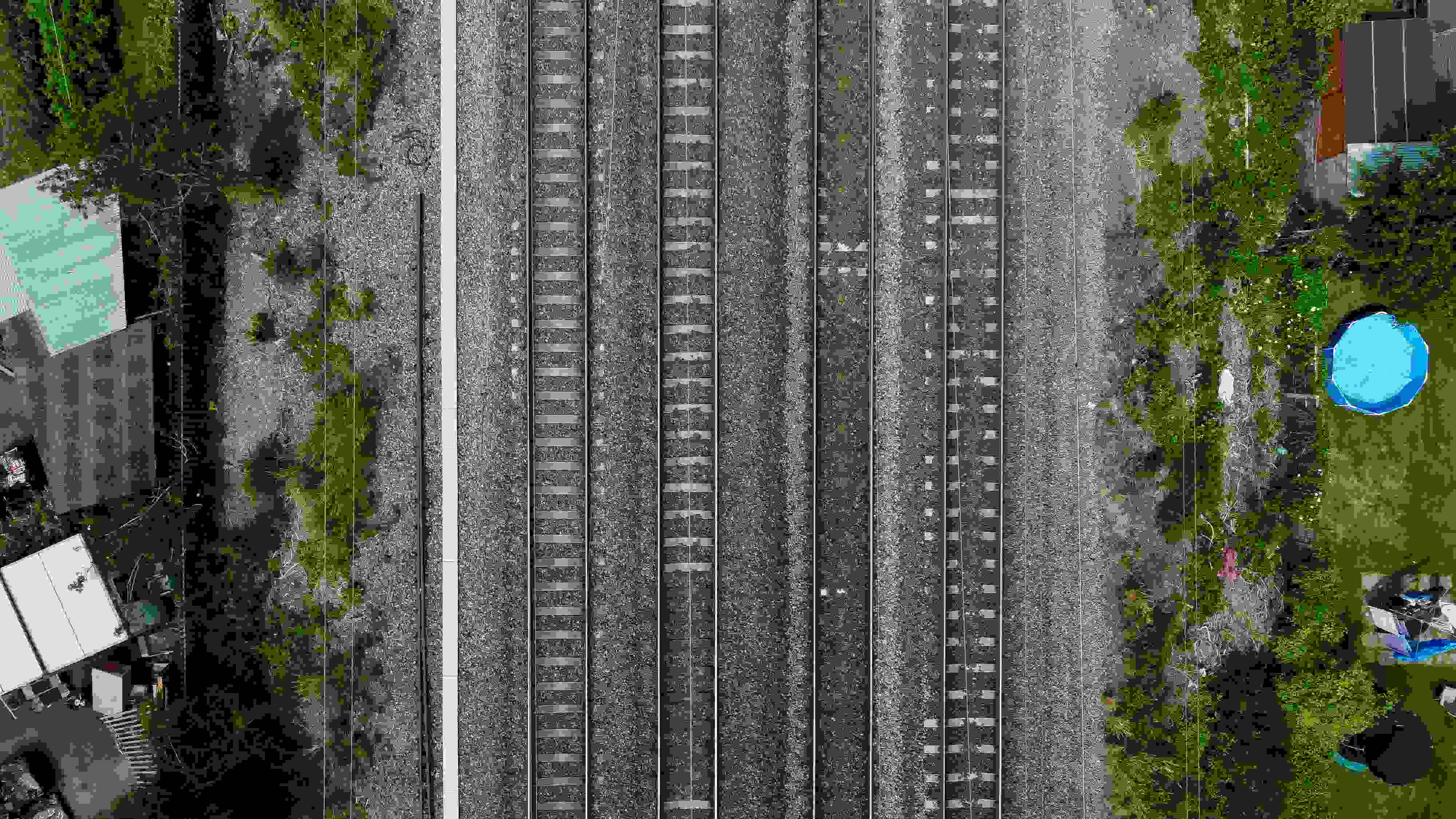 A bird-s eye view of part of the UK railway system, with multiple tracks lined by trees and buildings.
