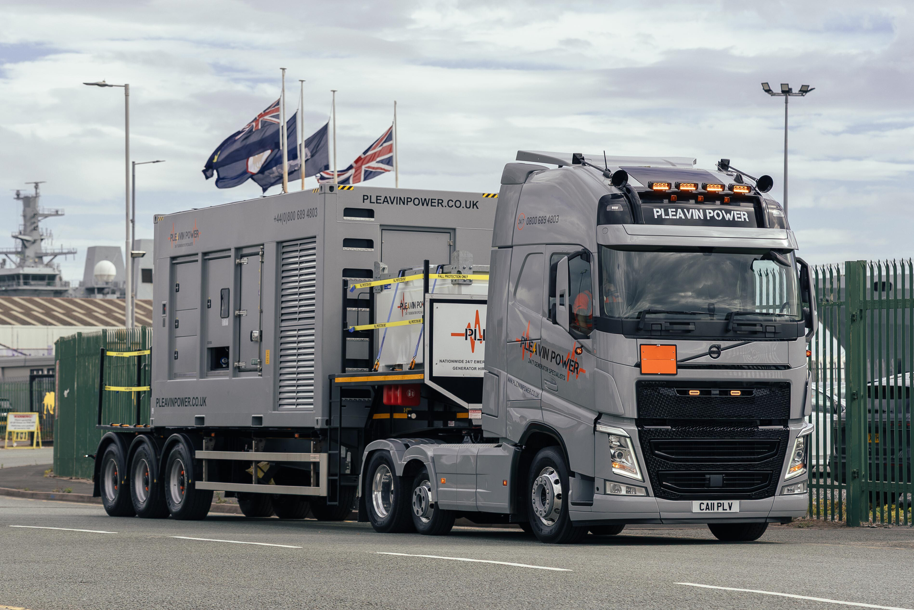 A HGV truck with pleavin power livery and a large emergency generator on the back.