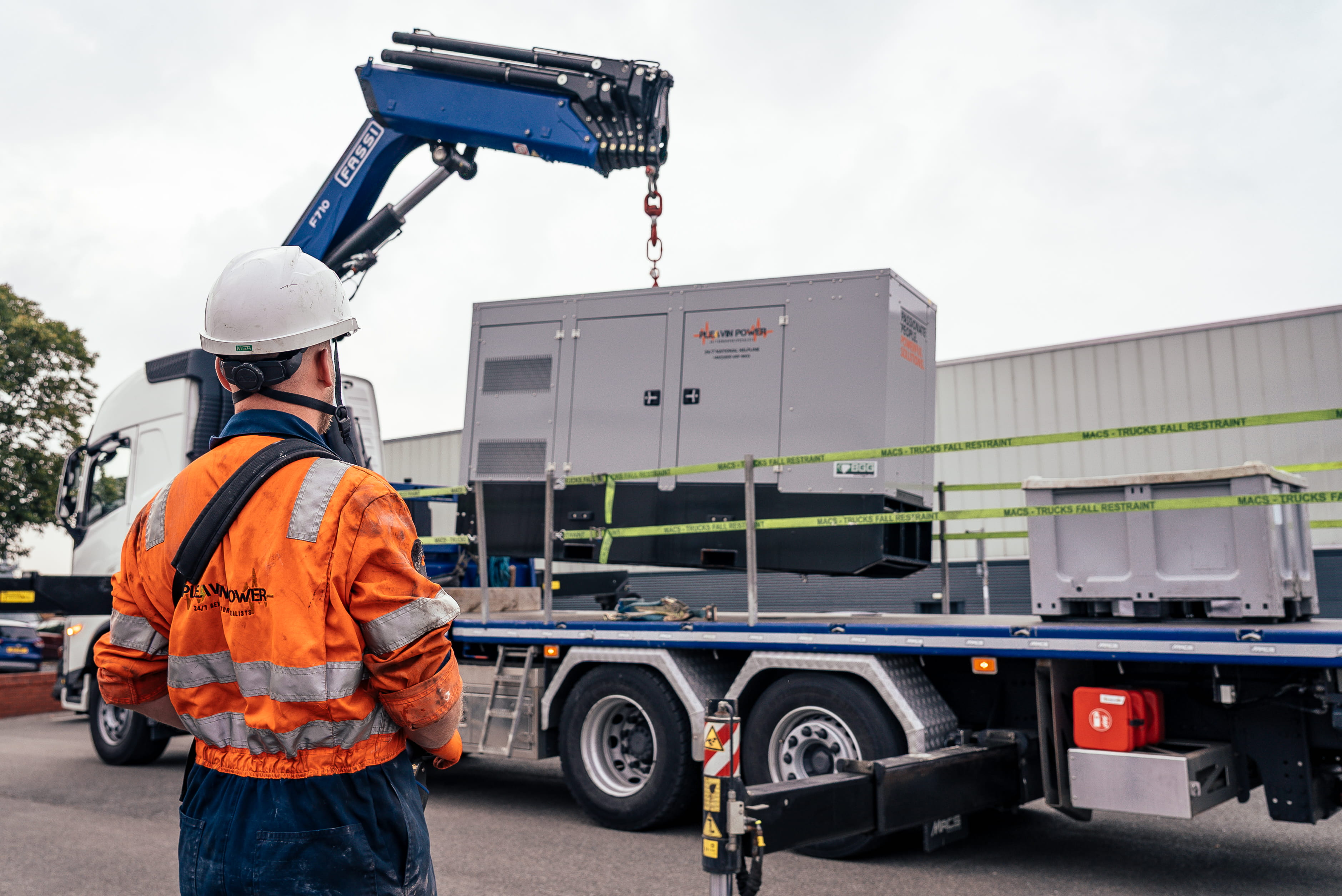 a pleavin power employee looking at a generator being lifted onto a trailer via a crane
