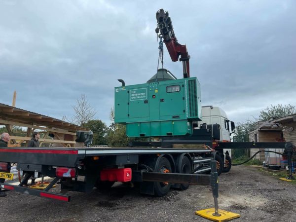 A van crane lifting a green generator onto the back on the van in preparation to arrive at an emergency generator servicing job.