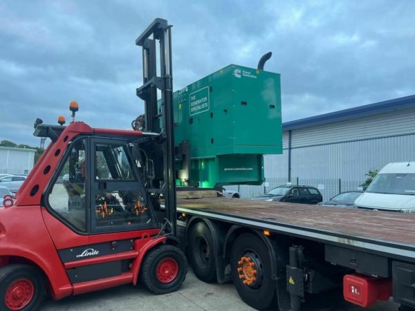 A red Linde forklift carrying a green Cummings generator onto a van.