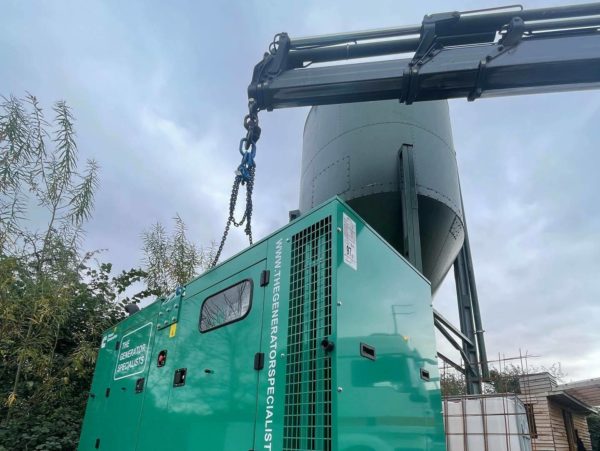 A green generator being lifted and placed onto the ground in preparation to complete a generator repair task.