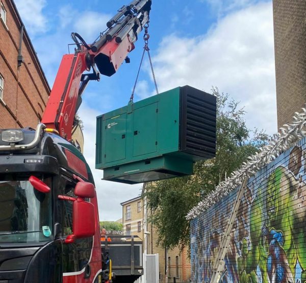 A red van lifting and placing a green generator onto the ground in order to start and complete a generator servicing job.