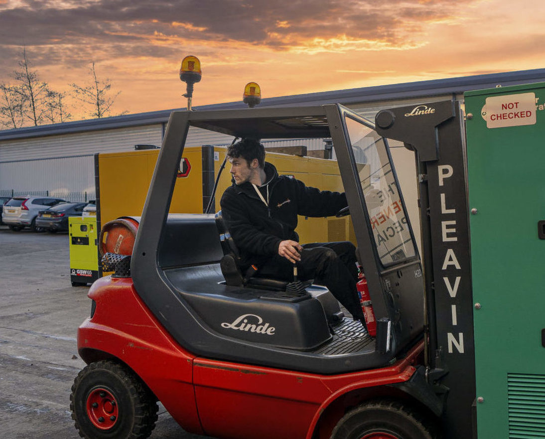 A Pleavin Power employee working on a red Linde forklift, using it to carry a red generator.