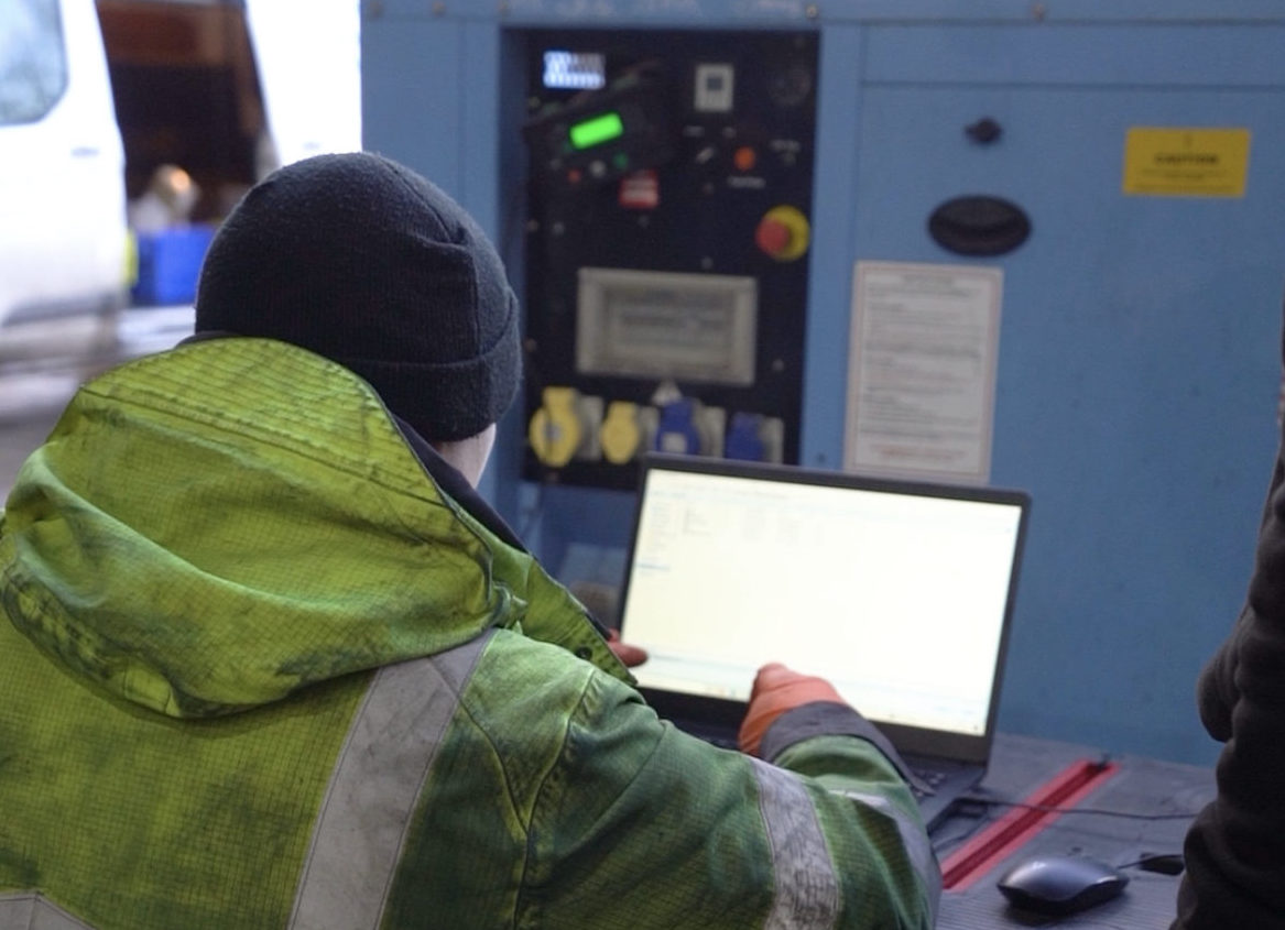 A Pleavin Power employee wearing a hi vis coat working on a laptop